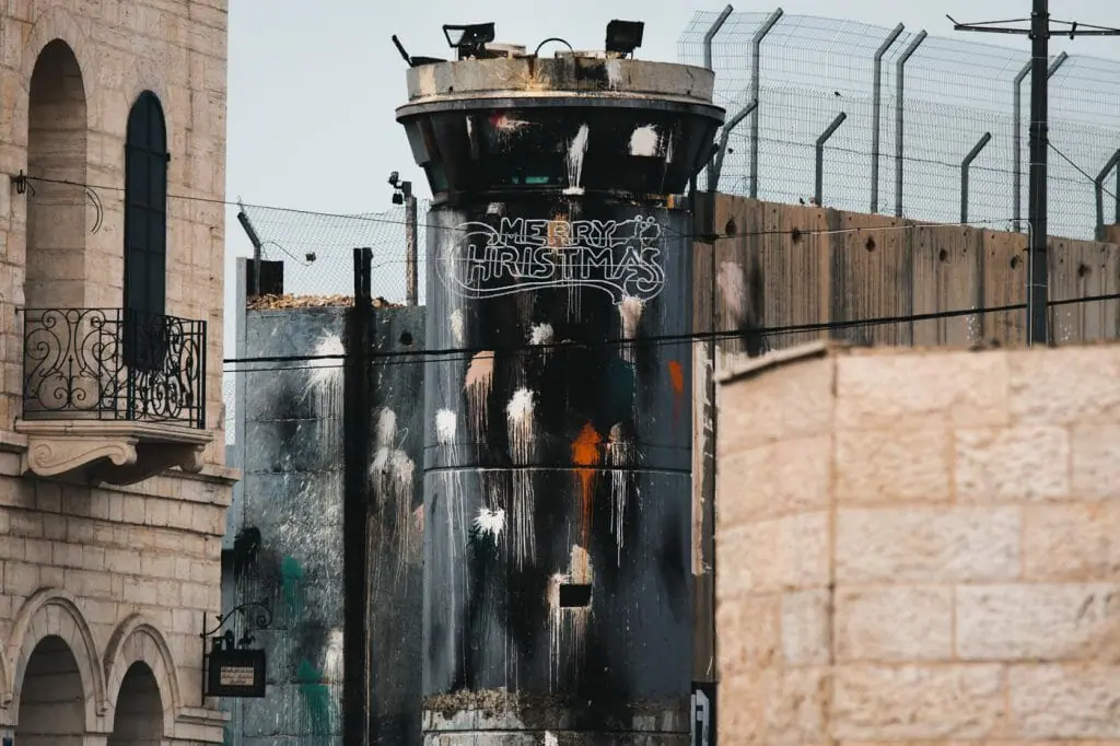 Christmas lights in Bethlehem, with the Separation Barrier and one of its towers in the background. The city is home to a significant Christian population and attracts tourists from around the world year round, particularly around Christmas time.