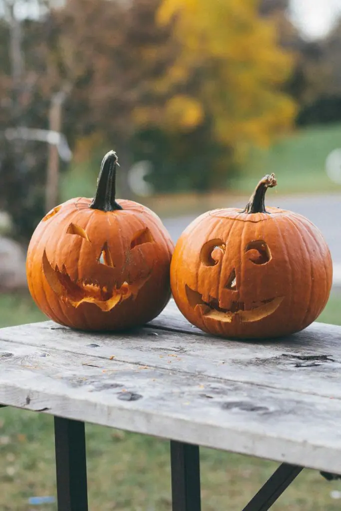 Two unlit jack-o-lanterns on a wooden table.
