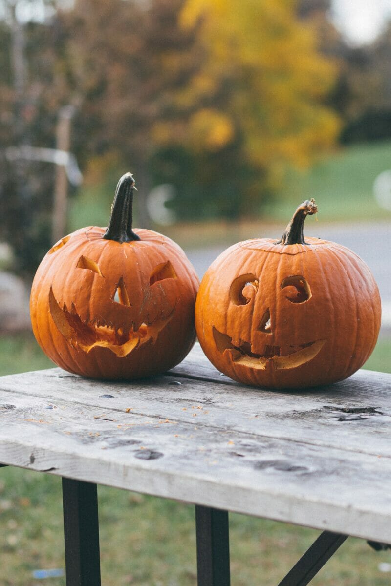 Two unlit jack-o-lanterns on a wooden table.
