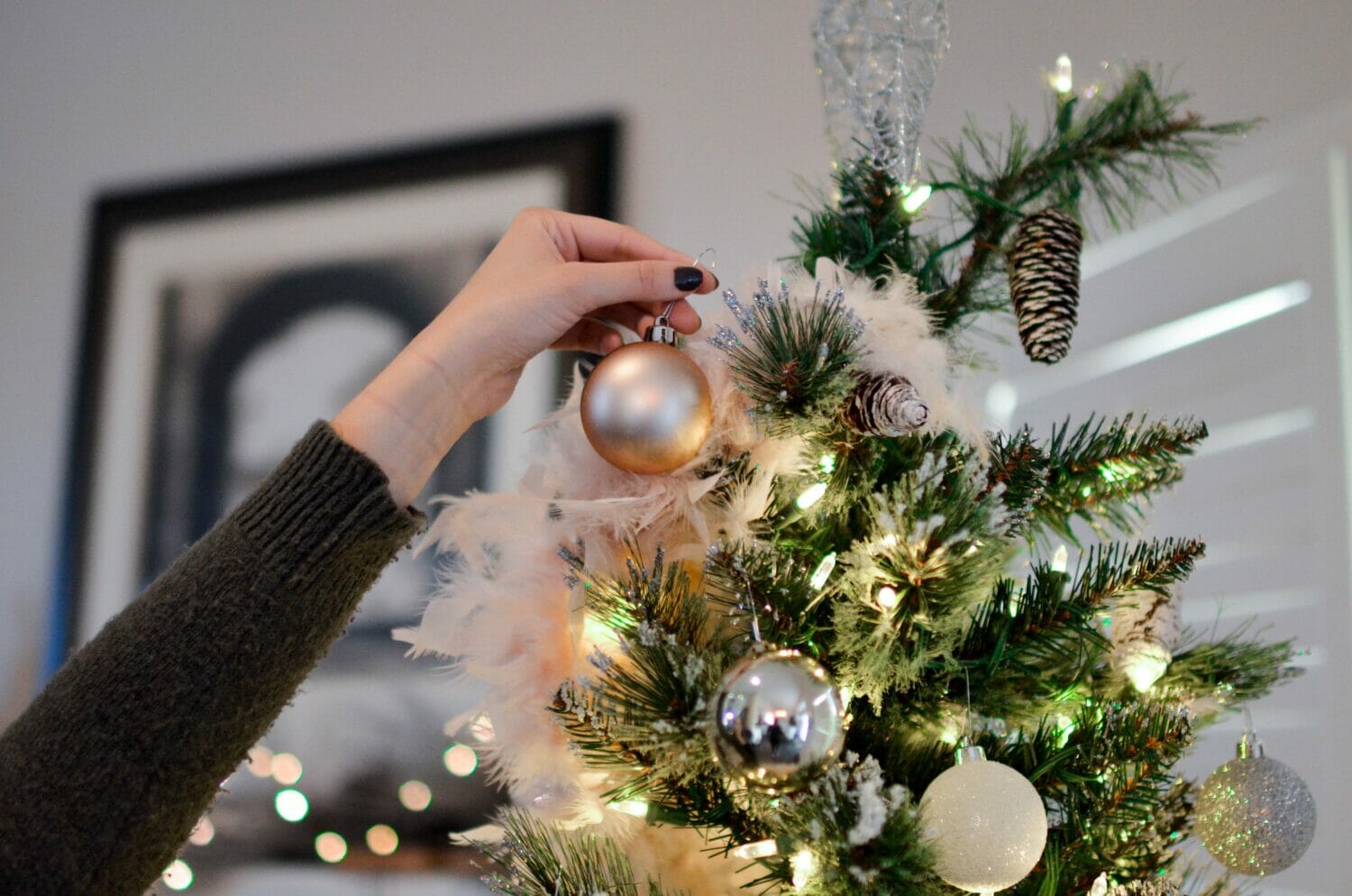 In this image: someone putting an ornament on a Christmas tree.