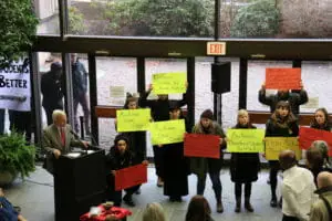 In this image: Protesters stood with their signs inside the building during MacKinnon’s speech.