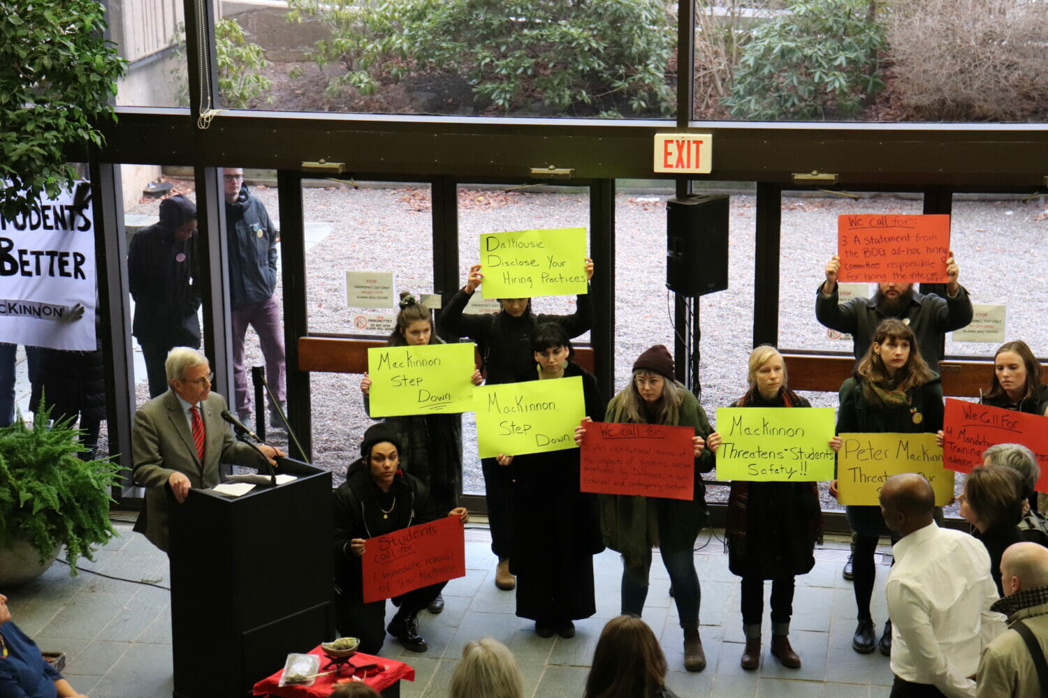 In this image: Protesters stood with their signs inside the building during MacKinnon’s speech.