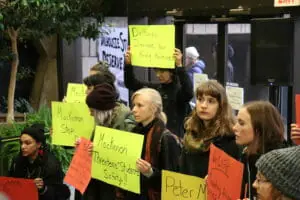 In this image: Dalhousie students stand in the Arts Centre holding signs protesting Peter MacKinnon.