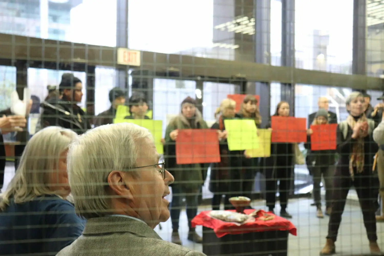 In this image: MacKinnon sits down after his speech, students hold signs in front of him.