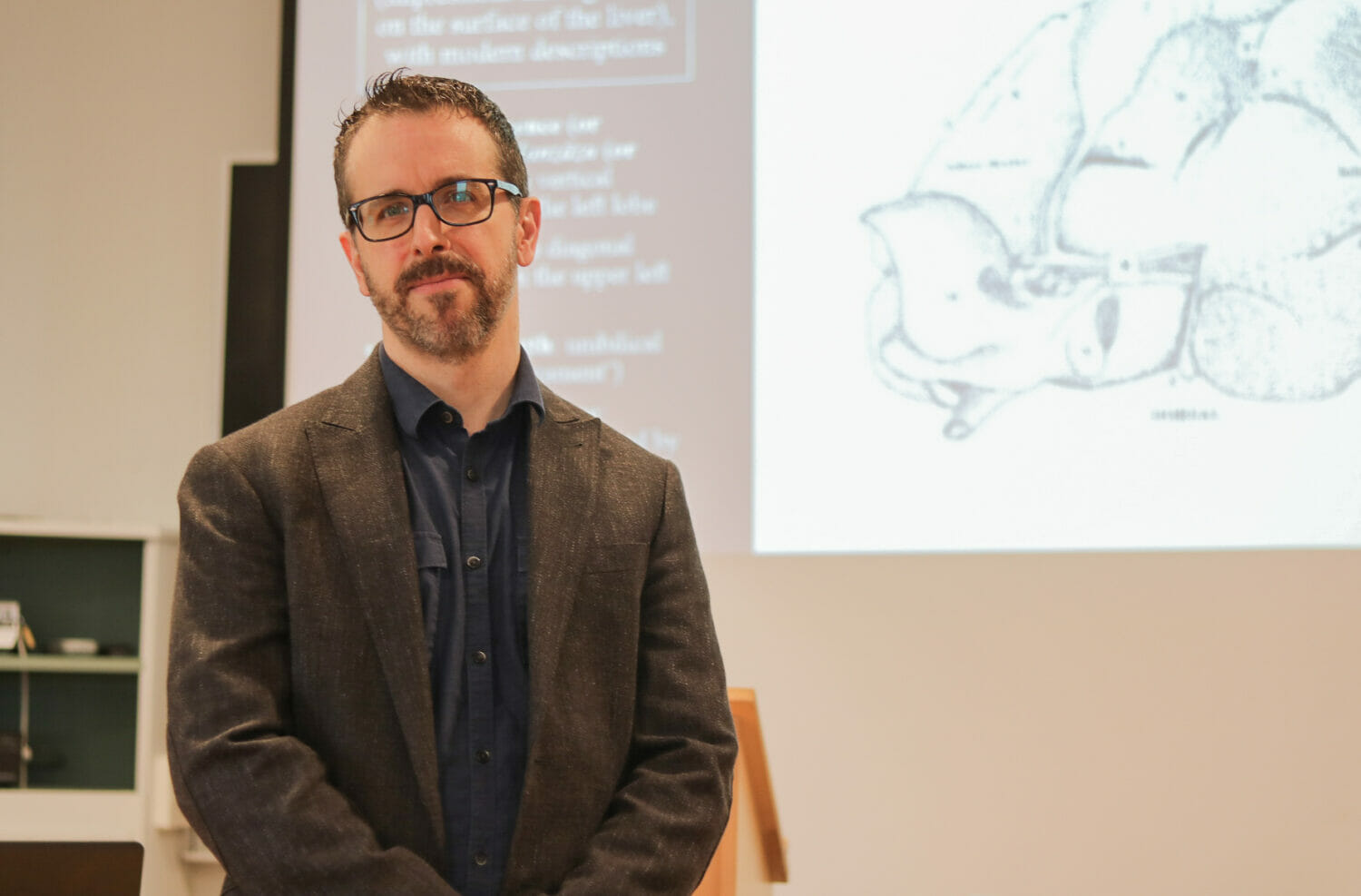 In this image: a headshot of Kyle Fraser in front of a presentation.