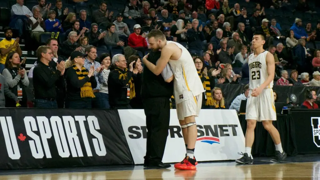 In this image: Mike Shoveller hugs Rick Plato while he and Kevin Duong walk off the court for the final time of their university careers.