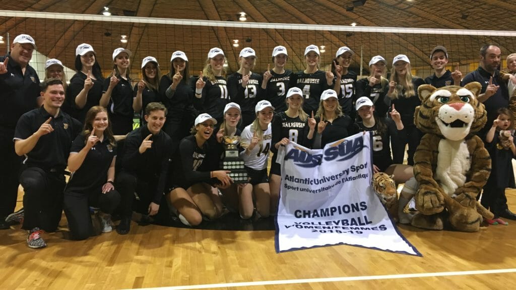 In this image: he Dalhousie women's volleyball team pose for a championship photo in front of the volleyball net at Dalplex on March 2.