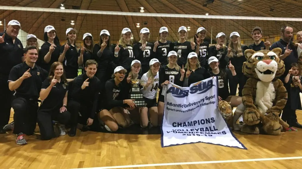 In this image: he Dalhousie women's volleyball team pose for a championship photo in front of the volleyball net at Dalplex on March 2.