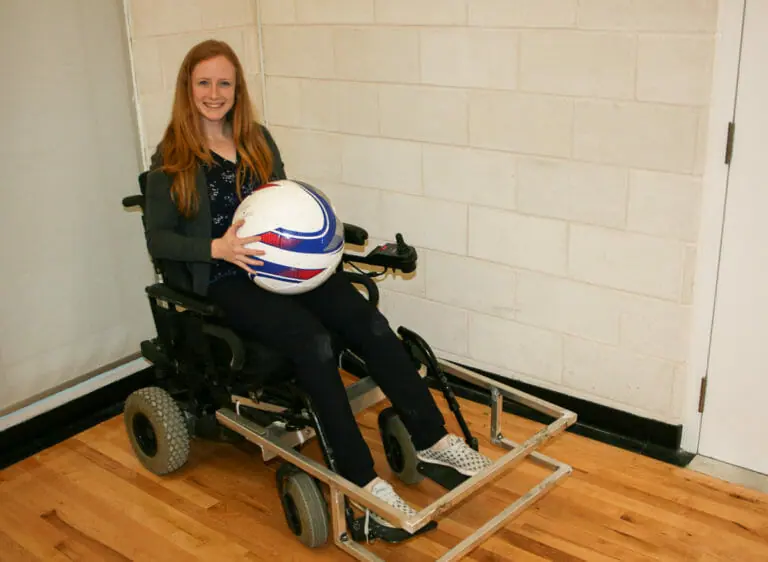 In this Image: Madison Campbell sits in a power wheelchair holding a powerchair soccer ball.