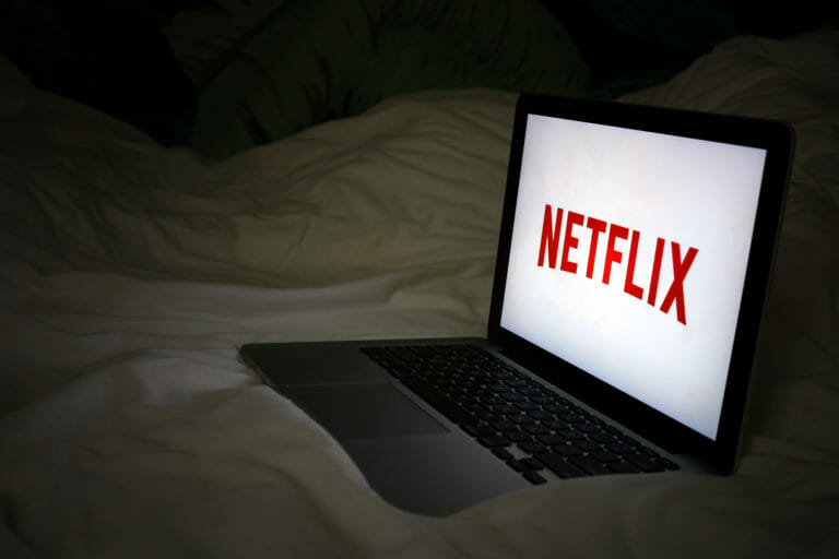 In this image: A laptop with Netflix playing on a bed.