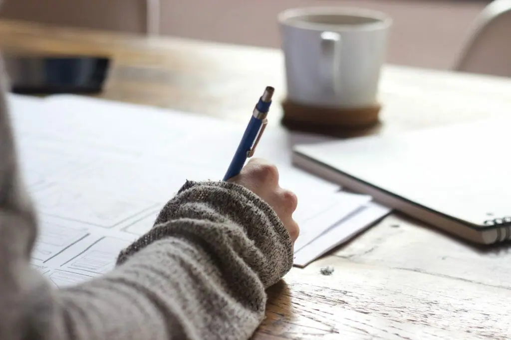 In this image: A person writes something with a pen on piece of paper.