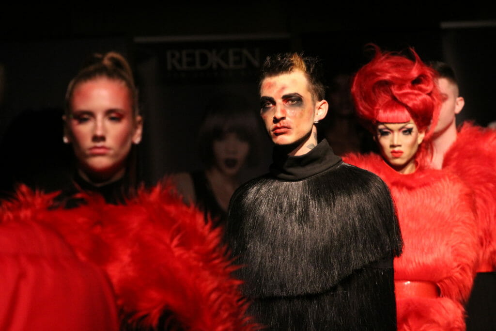 In this image: Three models model the runway in black and red.