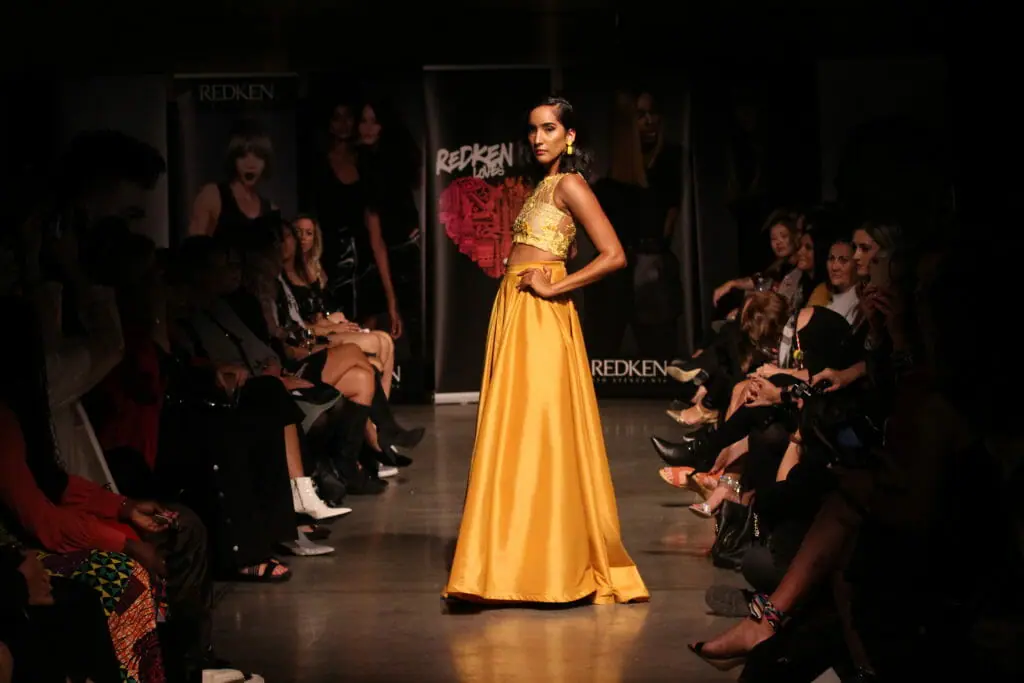 In this image: A model poses on the runway in a yellow gown.