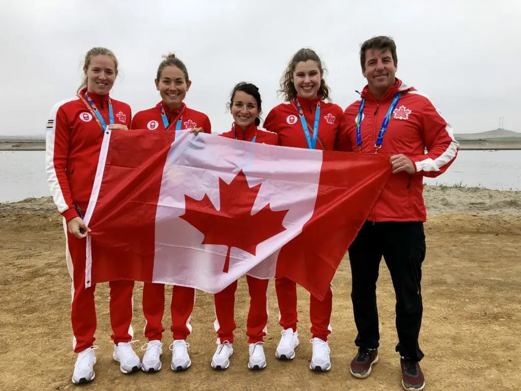 In this image: Five athletes from Team Canada pose with the Canada flag.