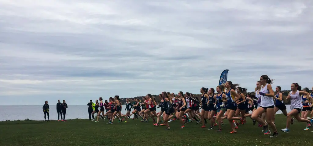 In this image: A large group of women start running in a cross country race.