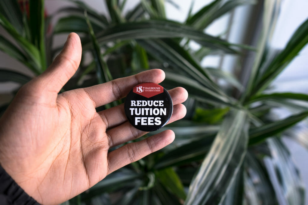 In this image: Someone holding a "Reduce tuition fees" DSU pin.