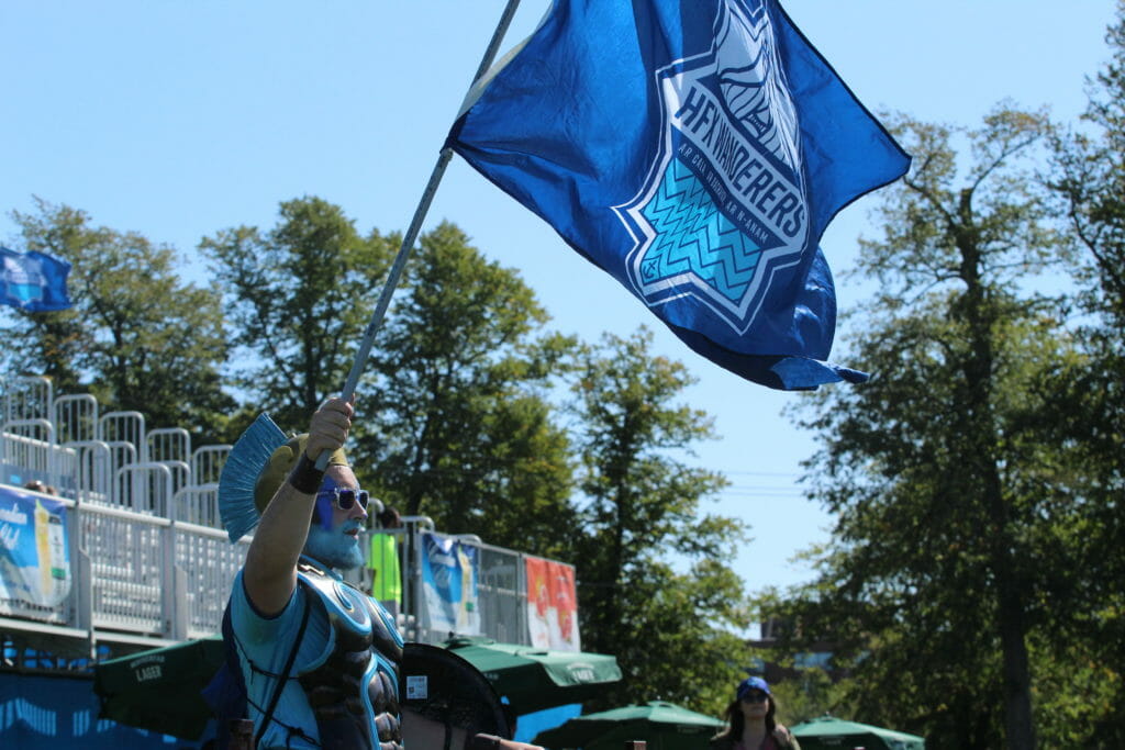 In this image: A Halifax Wanderer's mascot waves the team's flag.