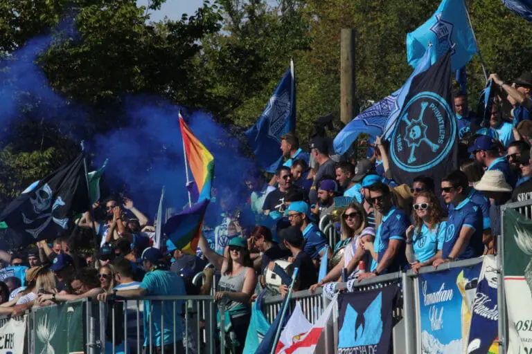 In this image: Fans watch from the sidelines with blue-coloured gear.