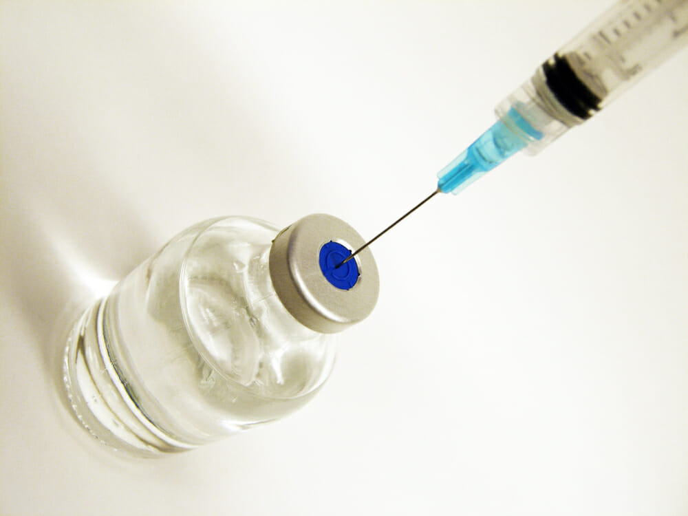 In this image: A needle goes into a vial.