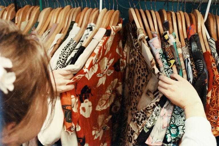 In this image: someone browsing through clothes on a hanging rack.