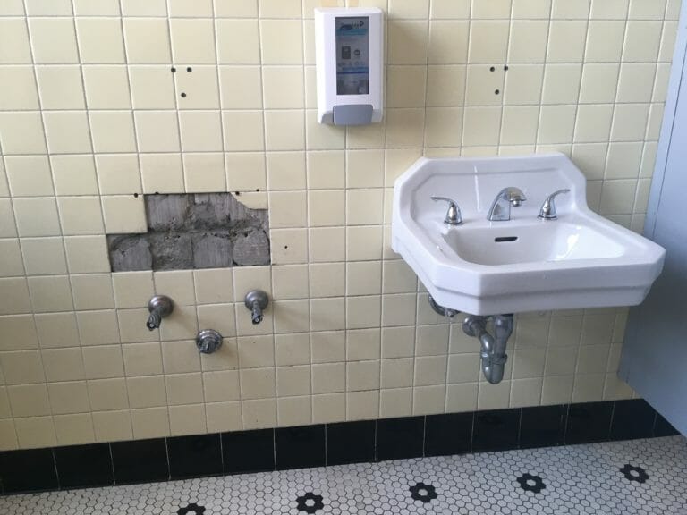 In this image: A women's washroom where one sink is displaced.