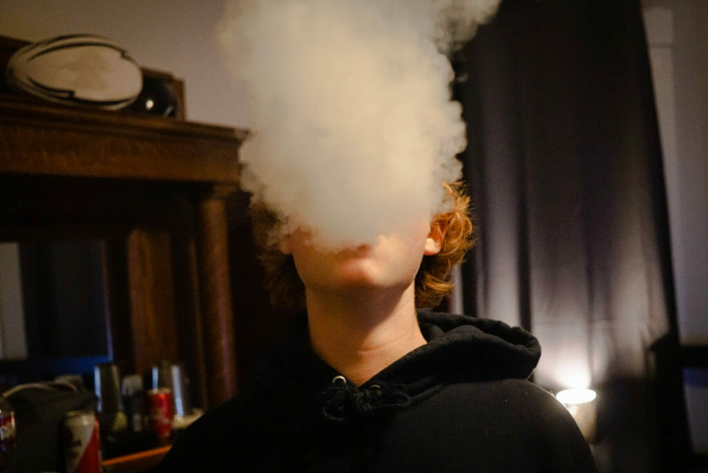 In this image: A person blows a vape cloud.