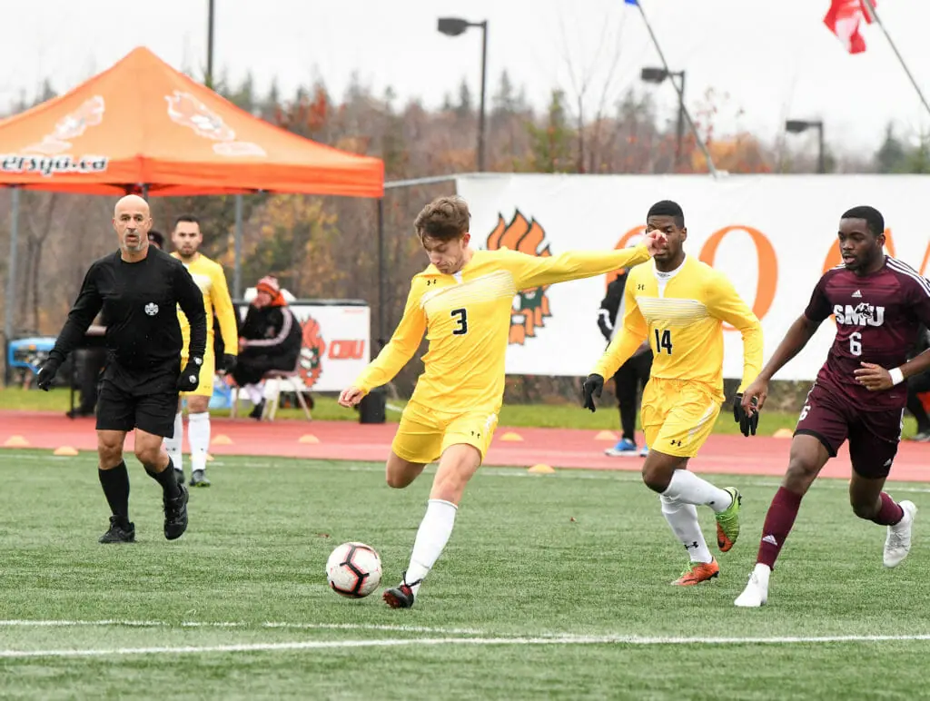 In this image: A Dalhousie Tiger goes to kick the ball during a game against the Saint Mary's Huskies.