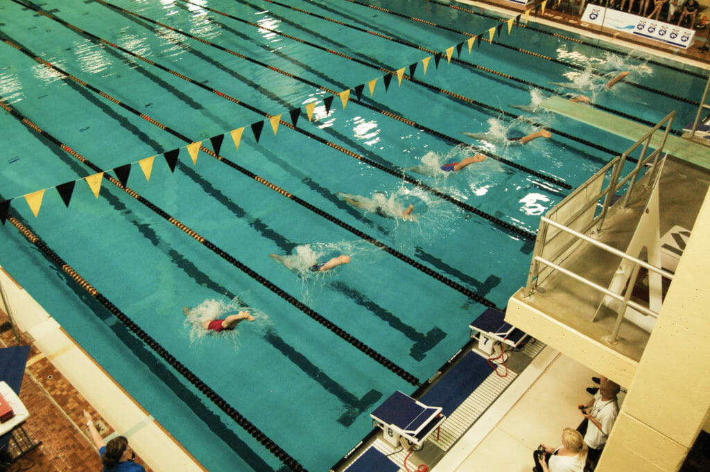 In this image: Swimmers dive into the Dalplex pool during an invitational.