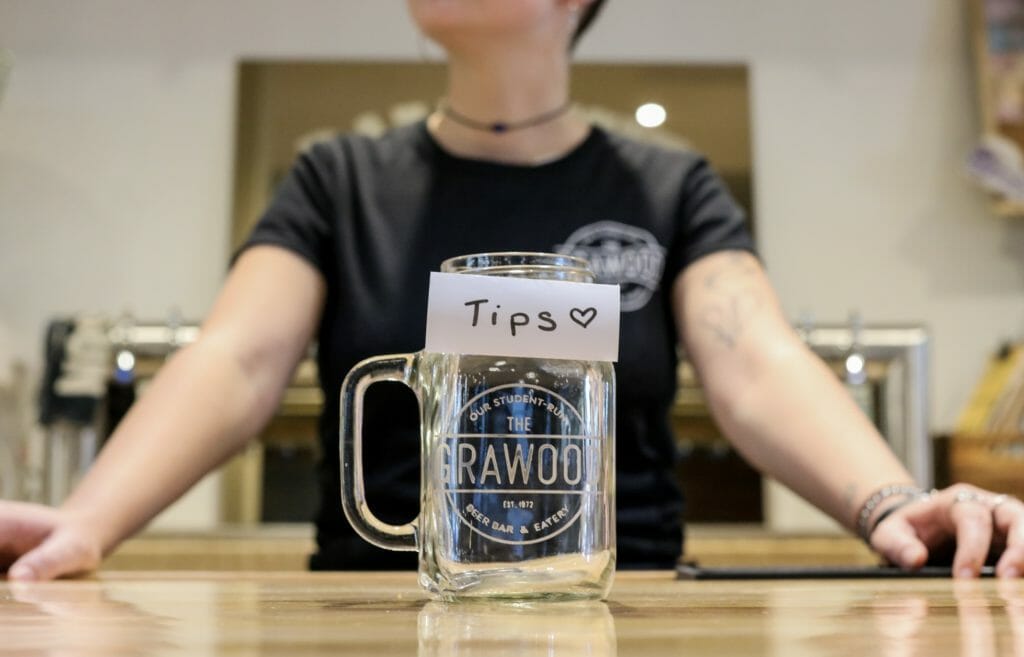 In this image: A Grawood employee stands behind an empty tip jar.