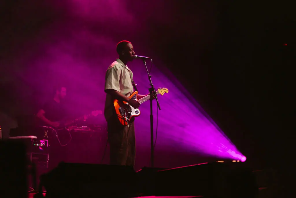 In this image: Daniel Caesar on stage playing guitar.