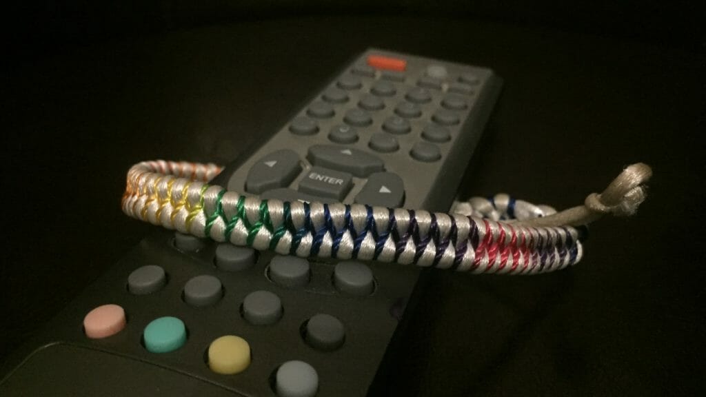 In this image: A remote control with a rainbow braclet tied around it.