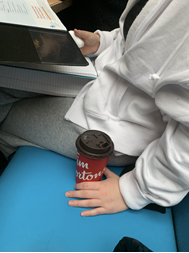 In this image: A person sits holding a Tim Horton's cup by their side.