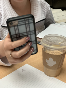 In this image: A person holds a cellphone beside a Tim Horton's drink.