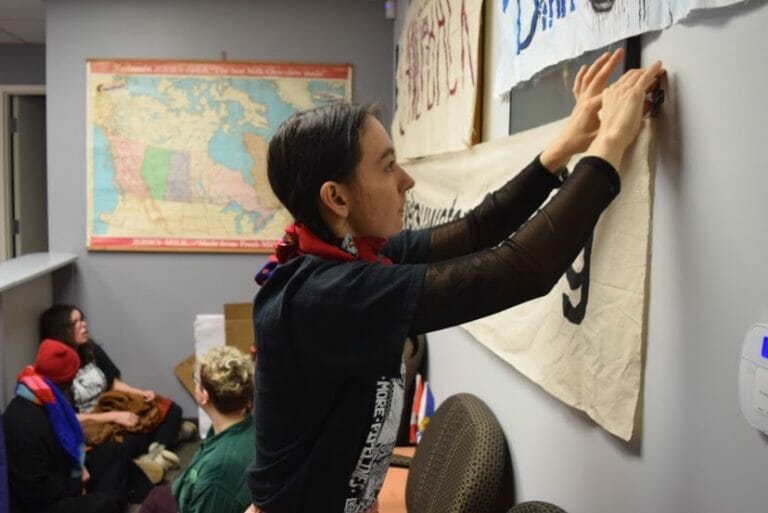 In this image: Naomi Bird hangs a sign in front of MP Andy Filmore's office.