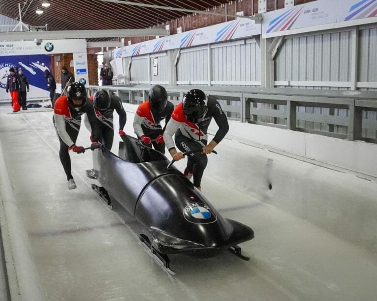 In this image: A bobsled teams pushes off at the start of a track.