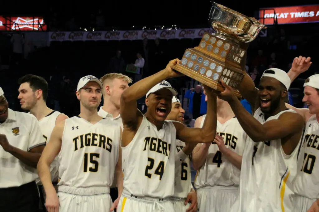 In this image: Shamar Burrows (left) and Jordan Wilson hold the AUS championships trophy among other Tigers.