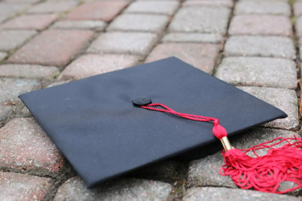 In this image: A graduation cap with a red tassel on the ground.