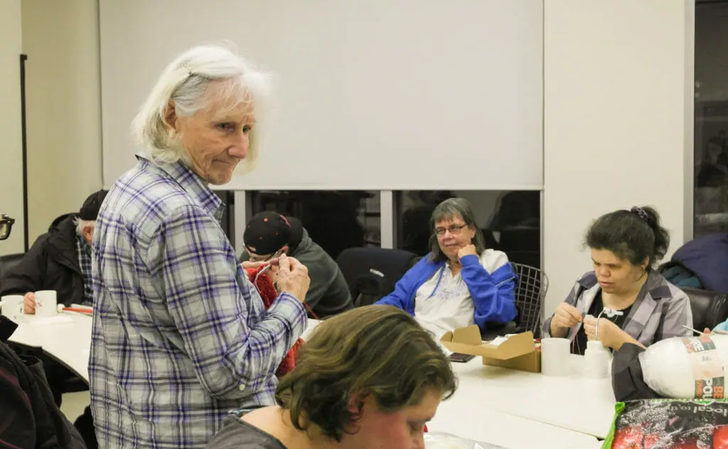 In this image: June Feswick stands at the knitting club.