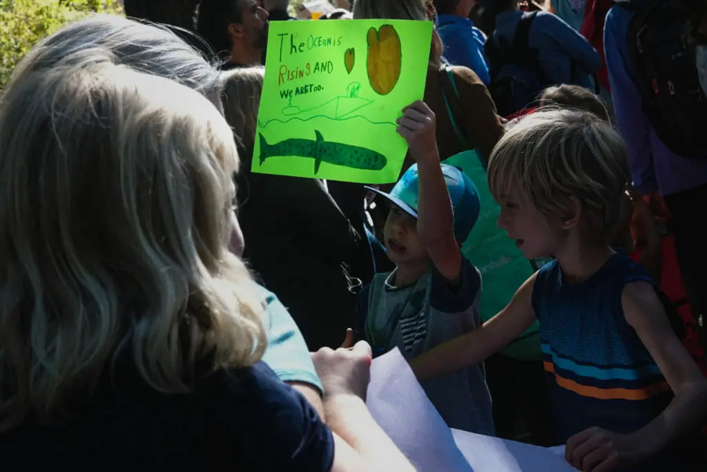 In this image: Two children with one of them holding a green sign.