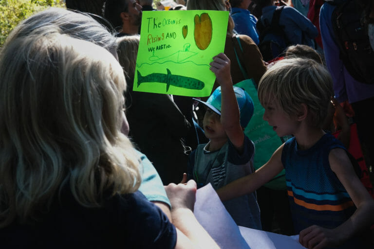 In this image: Two children with one of them holding a green sign.