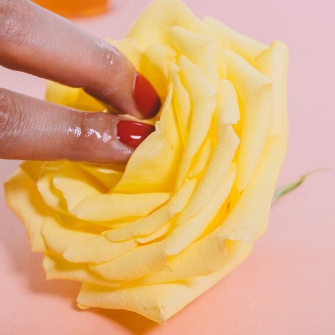 In this image: Two fingers touch the middle of a yellow flower.