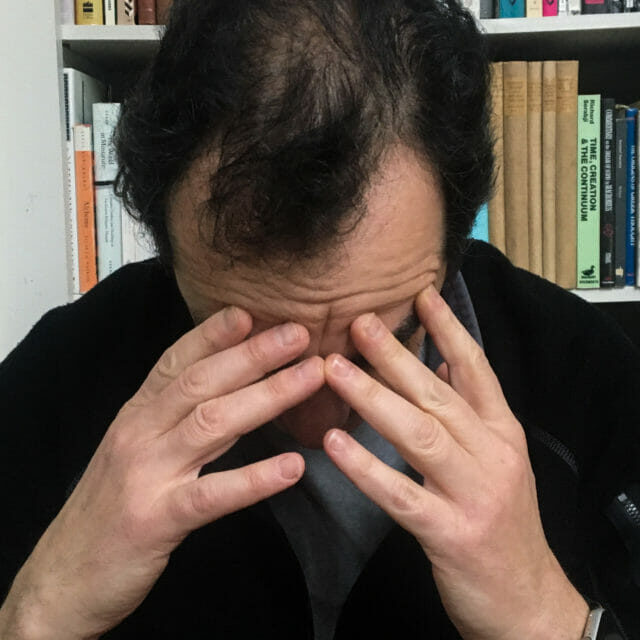 In this image: A person sits with their hands to their forehead.
