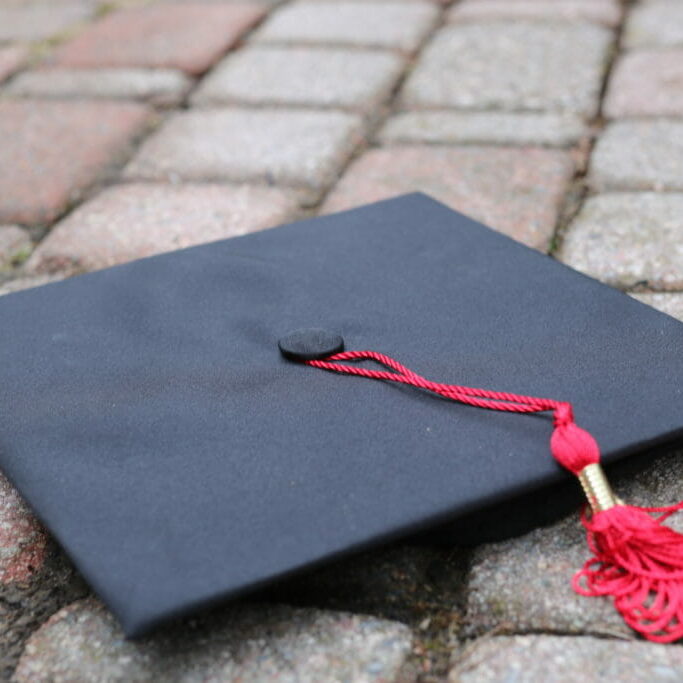 In this image: A graduation cap with a red tassel on the ground.