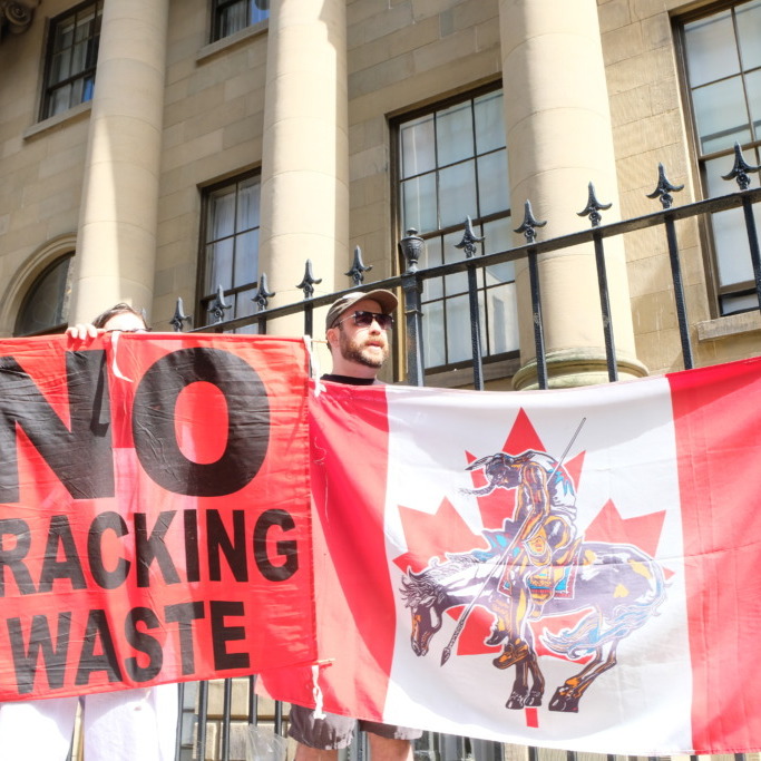 Protestors hold signs and flags outside Province House as part of a singing protest against Tim Houston's government on Sept. 8, 2026. (Dylan Follett/The Dalhousie Gazette)