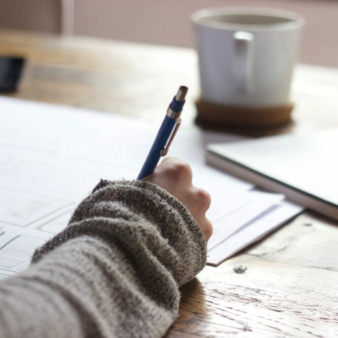 In this image: A person writes something with a pen on piece of paper.