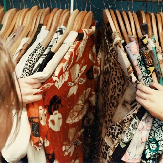 In this image: someone browsing through clothes on a hanging rack.