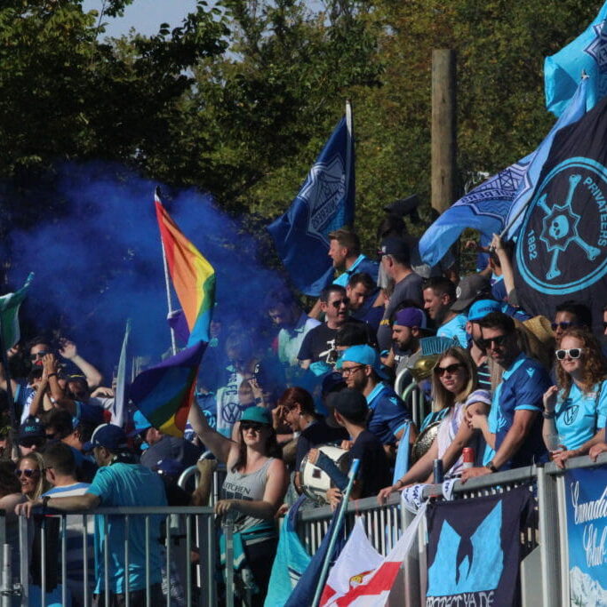 In this image: Fans watch from the sidelines with blue-coloured gear.