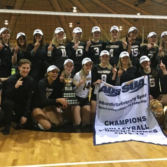 In this image: he Dalhousie women's volleyball team pose for a championship photo in front of the volleyball net at Dalplex on March 2.