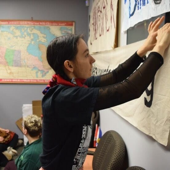 In this image: Naomi Bird hangs a sign in front of MP Andy Filmore's office.