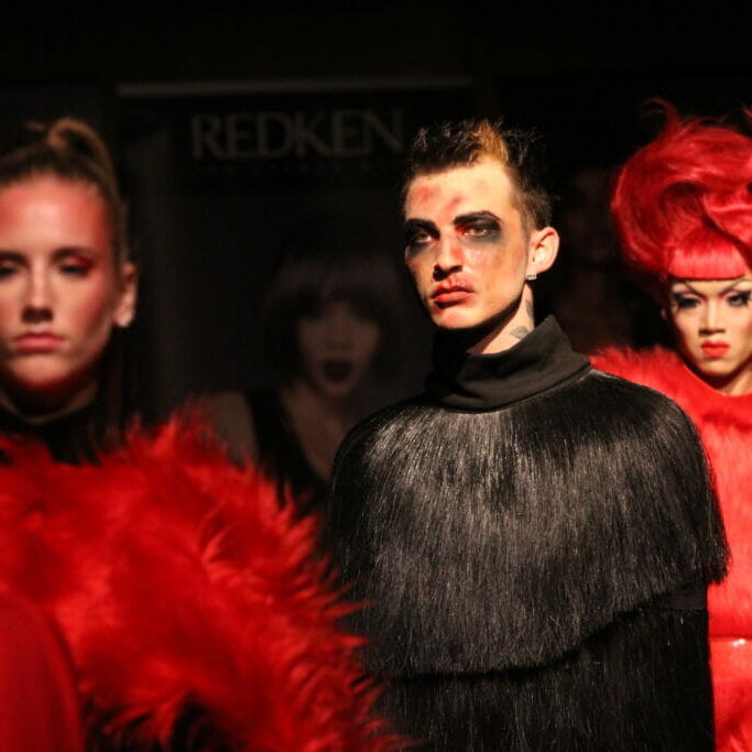 In this image: Three models model the runway in black and red.
